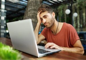 Hombre sentado frente a una computadora portátil, con una mano apoyada en la frente