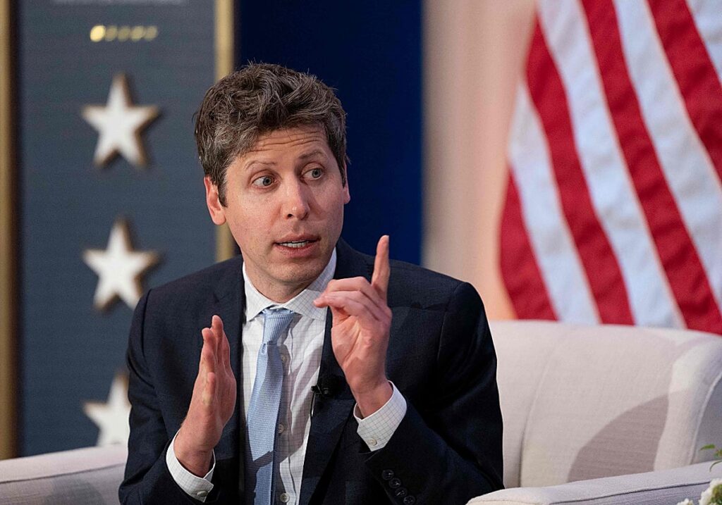 Hombre con traje gesticula sentado frente a una bandera de Estados Unidos.