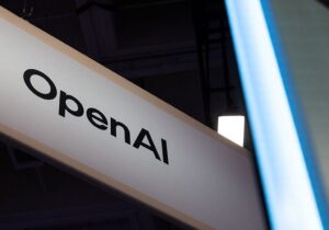 Letrero blanco con el nombre OpenAI, fotografiado en diagonal sobre un fondo oscuro.