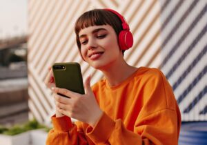 Mujer con auriculares rojos mira un teléfono móvil mientras sonríe.