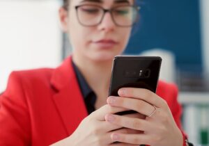 Persona con chaqueta roja y gafas sostiene un teléfono móvil con ambas manos.