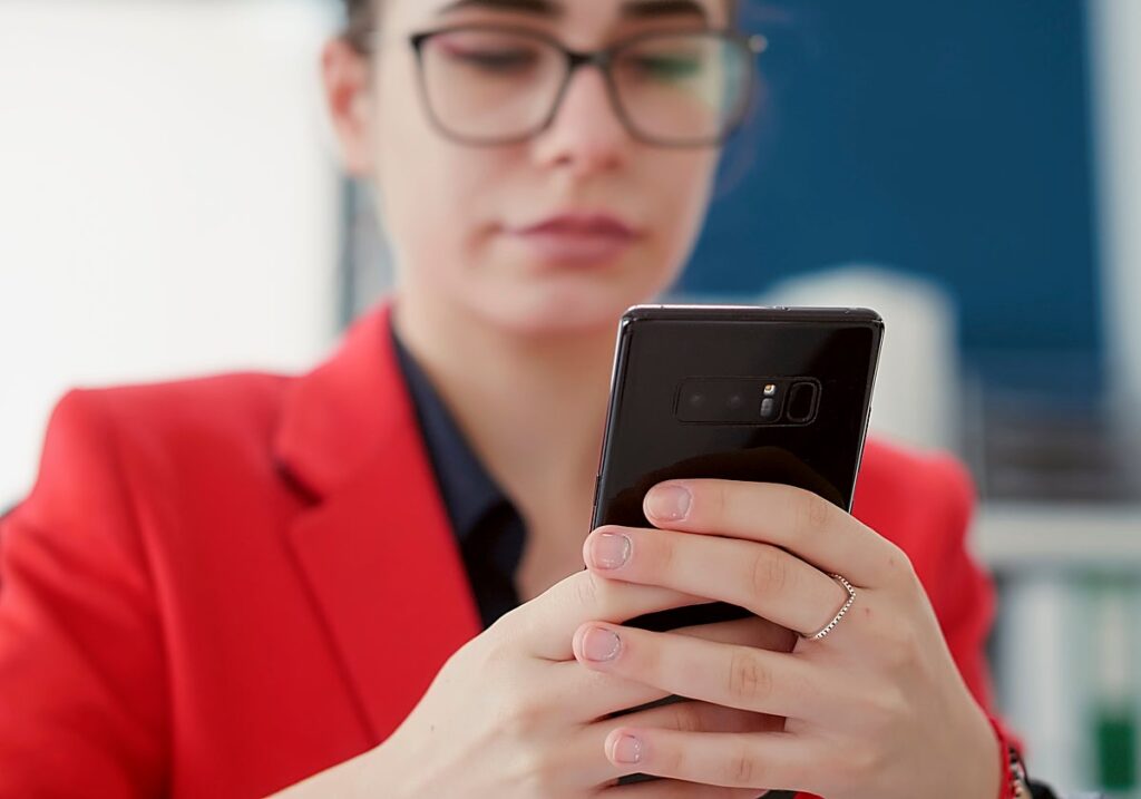 Persona con chaqueta roja y gafas sostiene un teléfono móvil con ambas manos.